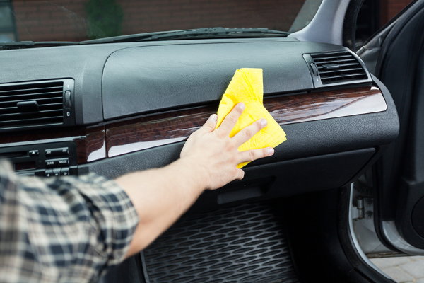 A man cleaning the interior of their car with a yellow rag. 