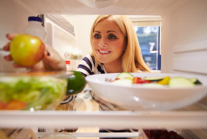 Woman reaching into a refrigerator for an apple