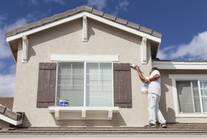 A man painting a outdoor windows and trim