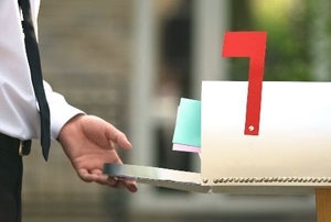 person in shirt and tie opening a mailbox with the flag up and mail sticking out