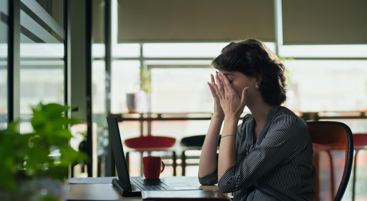 Tired woman sits at table holding her face.