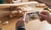hands holding a phone taking a picture of a wooden airplane toy