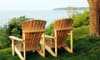 A pair of wood Adirondack chairs overlooking a body of water. 
