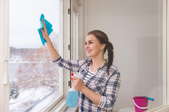 A woman cleaning a window with a spray bottle and rag. 