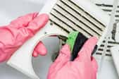 gloved hands with sponge cleaning bathroom fan vent