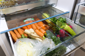 Produce door of refrigerator full of carrots, broccoli and other vegetables