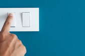 hand pressing light switch on bright teal wall