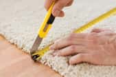 hands measuring and cutting a carpet with a tape measure and knife