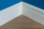 Corner of a room with blue wall, white baseboard trim and wood floors