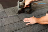 A roofing expert uses a nail gun to secure new shingles to the roof.