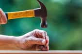 hands using hammer to drive nail into board