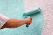 A homeowner painting a teal color over a stuccoed surface.