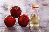 A trio of red apples next to a bottle of apple cider vinegar. 
