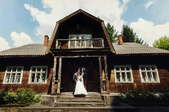 A bride and groom posing in front of a rustic farmhouse. 