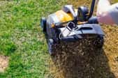 person pushing lawn aeration device over grass