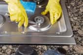 A pair of yellow gloves cleaning a metal stove top. 