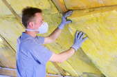 A man wearing gloves and a dust mask working with insulation in an attic.