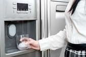 A woman uses a water dispenser in a fridge.