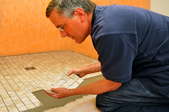 Man repairing a sheet of mosaic ceramic tiles on a shower floor.