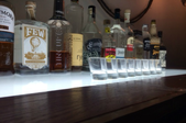 A row of shot glasses with a row of bottles behind them.
