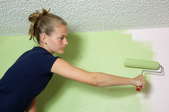 A painter rolling green paint onto a white wall.