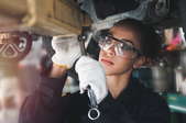 woman with goggles and gloves working under a car