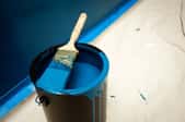 A paintbrush dipped in blue paint sits across the top of a blue paint can.