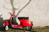 red gas scooter against a wall with a tree shadow
