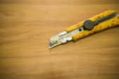 Stained, yellow utility knife laying on a piece of wood.