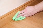 A hand wiping a baseboard with a green cloth. 
