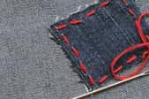 red thread holding a blue patch on denim fabric