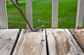 A crowbar is being used to pull lifted nails out of a worn, peeling deck.