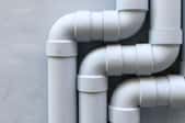 three sets of white PVC pipes against a gray wall