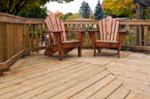 Two wooden Adirondack chairs on a backyard deck.