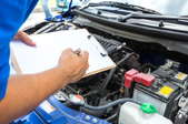 A man holding a checklist looking at a car engine. 