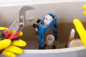gloved hands fixing open toilet tank with plumbing wrench