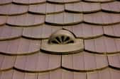 A matching roof vent in the midst of brown shingles.