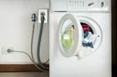 Hoses and and cords connect a washer to a wall.