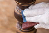 gloved hand removing wood stain from furniture leg