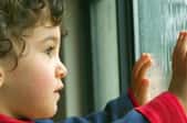 Child with hands on a window, looking out.