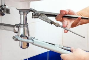 two hands adjusting valves under a sink using tools