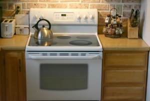 A white electric stove with a kettle on the burner.
