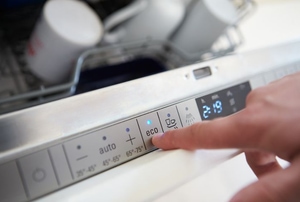 A eco-friendly dishwasher with someone pressing a button on the front. 