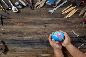 A pair of hands holding a small globe with a bunch of tools surrounding it.