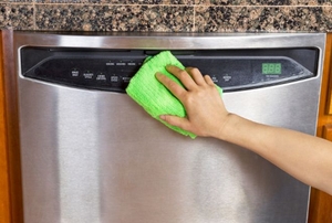 Wiping down the front panel of a stainless steel dishwasher.