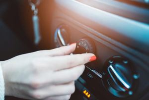 A female hand adjusting the vent on a car dashboard.