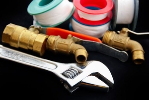 A grouping of plumbing tools including thread seal tape, a wrench, and pipe fittings.