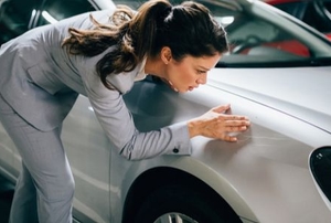 an upset woman inspects a scratch on her car in a parking garage