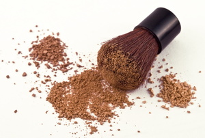 A bronzer brush with bronzer powder against a white background. 