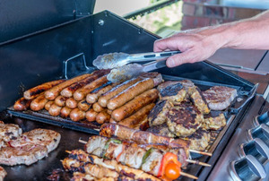 an open grill with a stack of hot dogs and other meats cooking.